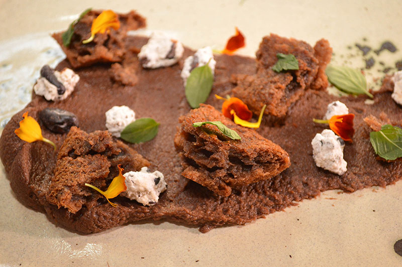 El postre lleva productos provenientes todos de la amazonia bolivia. En la base del plato un ganache de chocolate, los trozos son como una masa intermedia entre el flan y el bizcocho, adornados con garrapiñadas de granos de café.