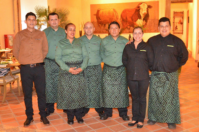 El equipo de servicio, con delantales elaborados con tejidos indígenas. Y al fondo otra imponente obra de Koki, un homenaje al ganado del Chaco.