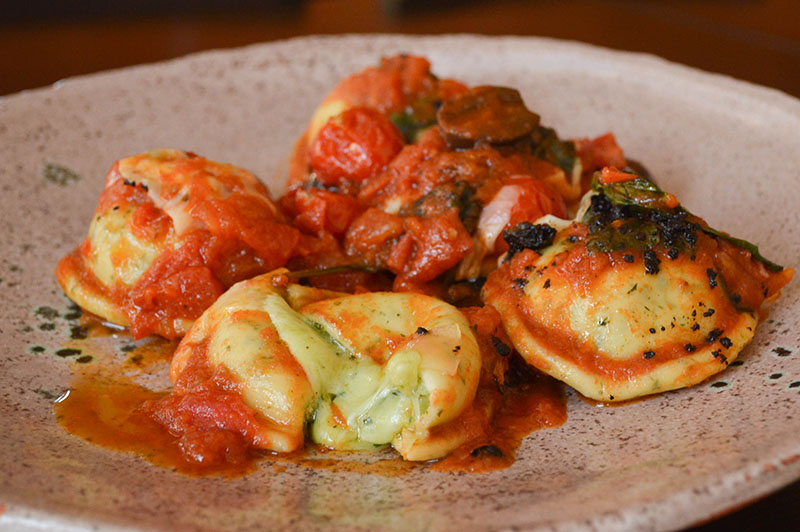 Ravioles caprese, de elaboración casera, rellenos con muzzarella. La salsa está preparada en un salteado de cherry, oliva, tomate y albahaca. La masa lleva en su composición un poco de albahaca para intensificar el sabor.