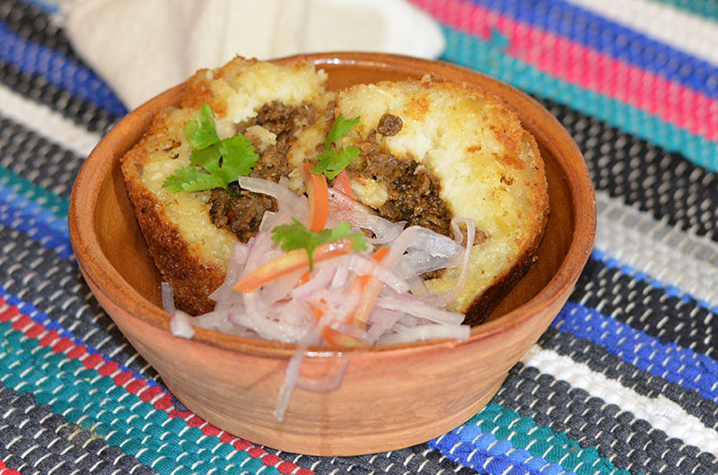 Aquí se fuionan la mandioca como producto oriundo y la técnica del salteado de carne como relleno, acompañas con la salsa criolla, sin olvidar el toque de sabor del ají panca.