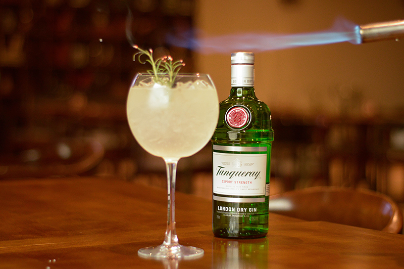 El gin tónic clásico lleva una medida de Tanqueray, hileo y agua tónical. A veces un twist de limón. En esta versión el barman le agregó un poco de romero que fue sopleteado para avivar su aroma.
