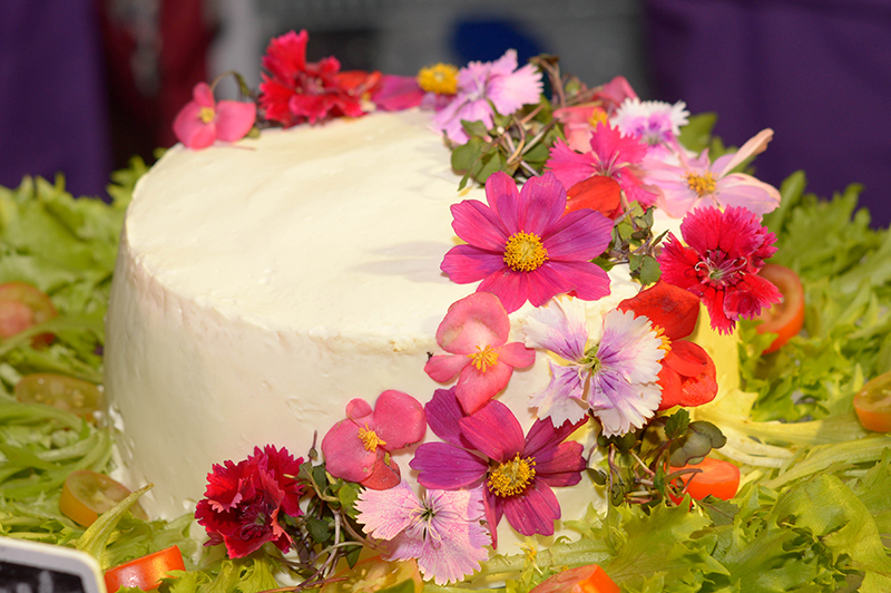 la vista luce como una torta decorada con flores comestibles, como muchas que se ofrecen en el mercado. Pero su interior revela un contenido diferente. Porque se trata de una ensalada con forma de torta.