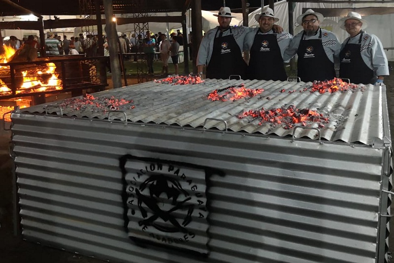 El equipo paraguayo que asistió al Festival del Asado con Cuero, en la Argentina. Frente a ellos, una caja de chapa en cuyo interior está la parrilla con la carne asandose con fuego por debajo y arriba.