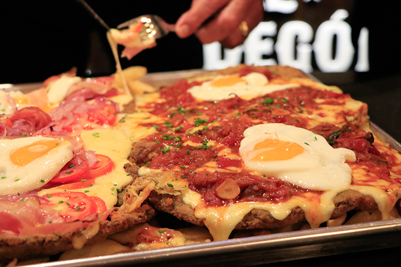 Colchón de papas fritas, milanesa XXL, rodajas de tomate, jamón, panceta, cebolla caramelizada y huevos fritos. Asi es la mejor milanesa de bodegón de Buenos Aires que ya puede comerse aquí.
