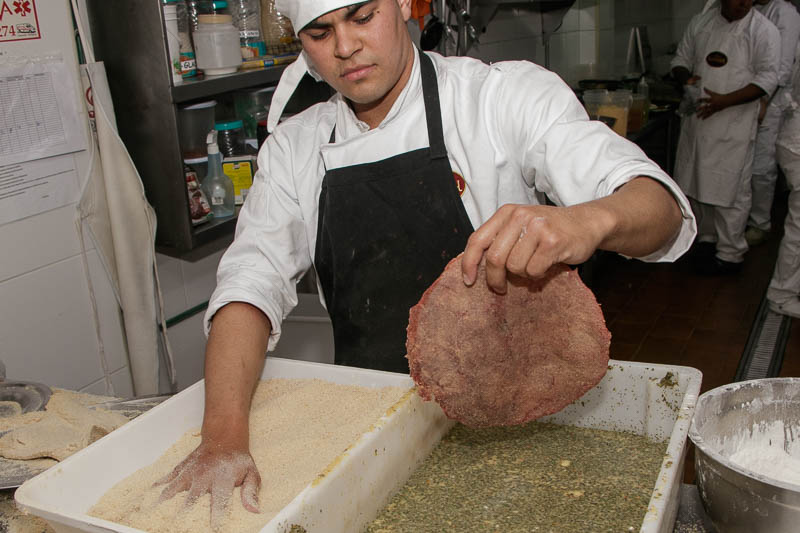La milanesa está por ingresar a un baño de huevo, leche y condimentos varios. Luego se apana y va directo a la freidora. El tamaño XL lleva dos de esas milanesas redondas.
