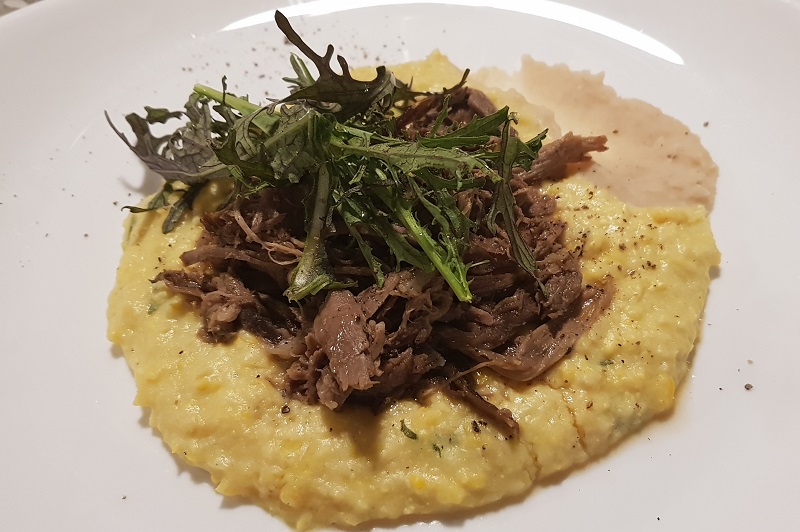 Cordero braseado con puré de choclos y crema de alubias, con hojas de rúcula morada.