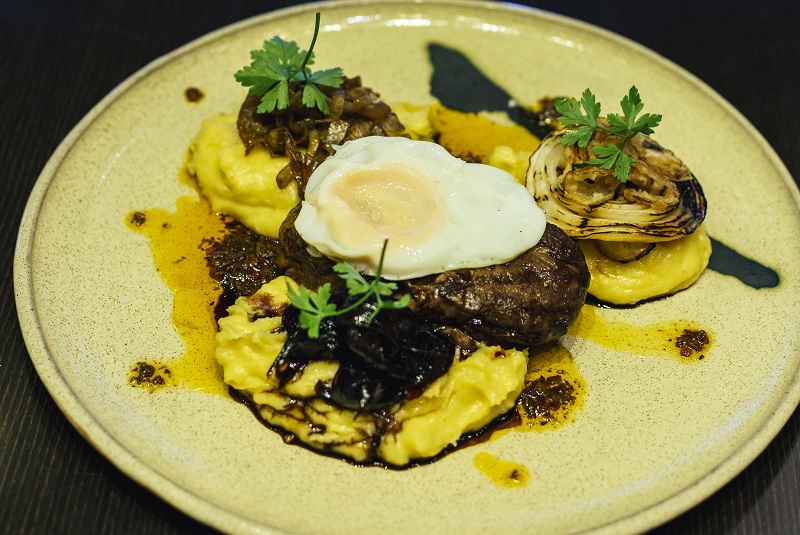Churrasco de lomito con puré de papas, con gruyere y diferentes texturas de cebollas.