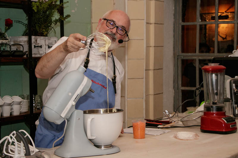Osvaldo Gross mostrando la consistencia de la crema preparada con el pequeño robot de colos gris que tiene enfrente. NGO conmemoró así los 100 de la batidora KitchenAid.